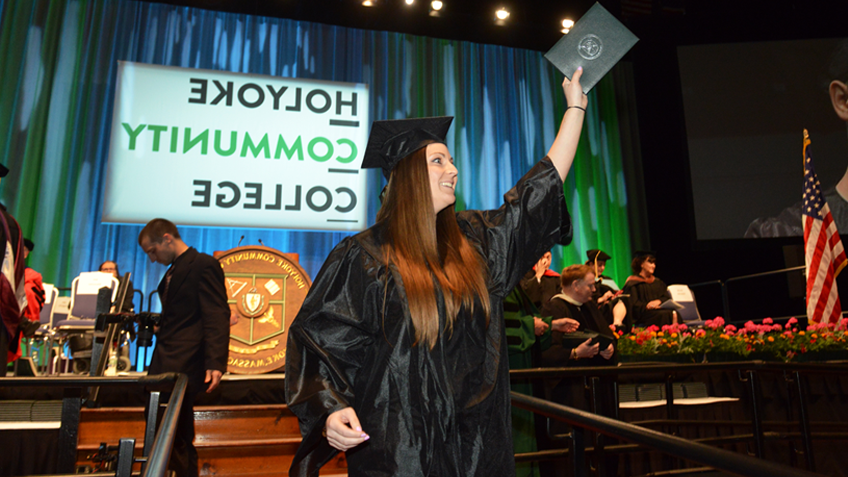 在毕业典礼上，一位面带微笑的女韦德买球网站毕业生戴着她的帽子和长袍，拿着她的毕业证书